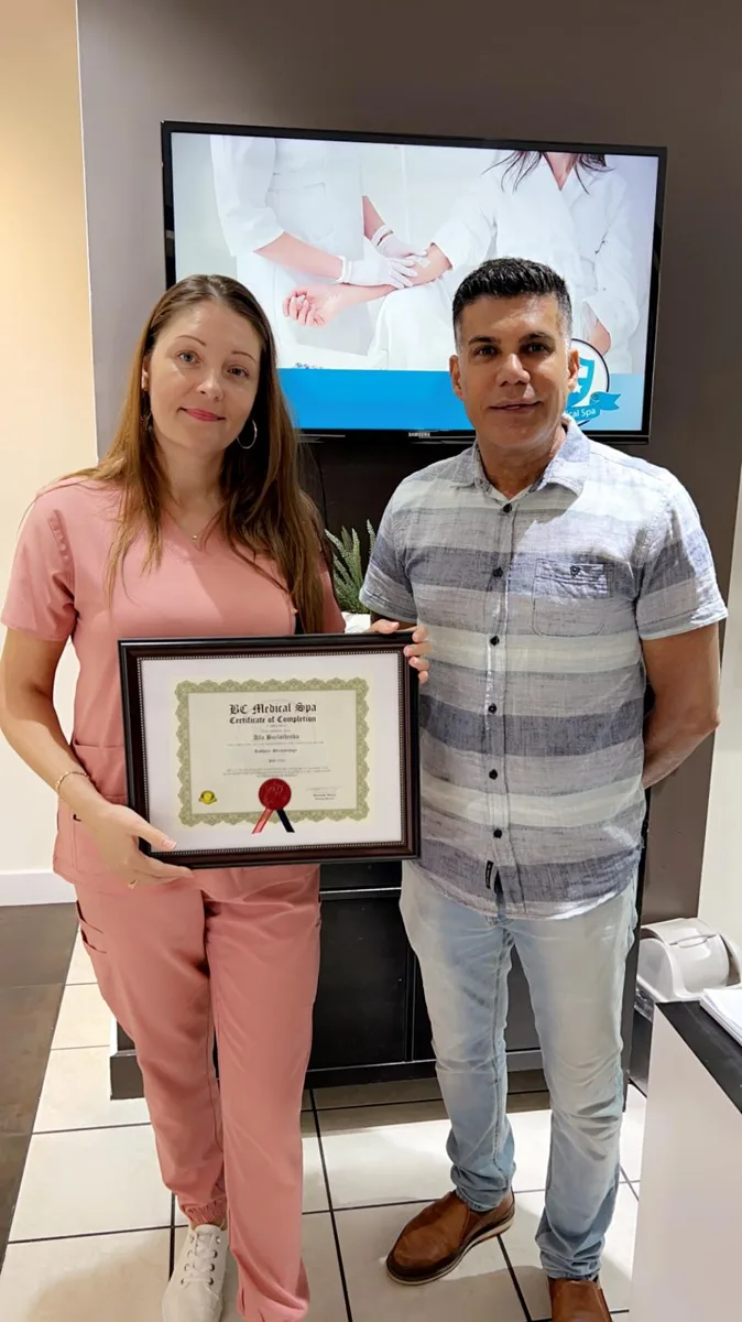 BC Medical graduate holding their framed certificate with their instructor at the Coquitlam campus